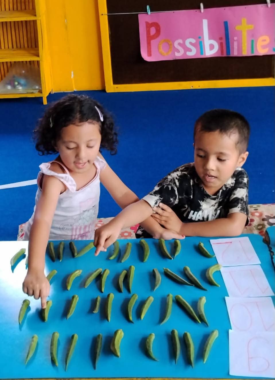Two children counting rows of okra laid out on the table