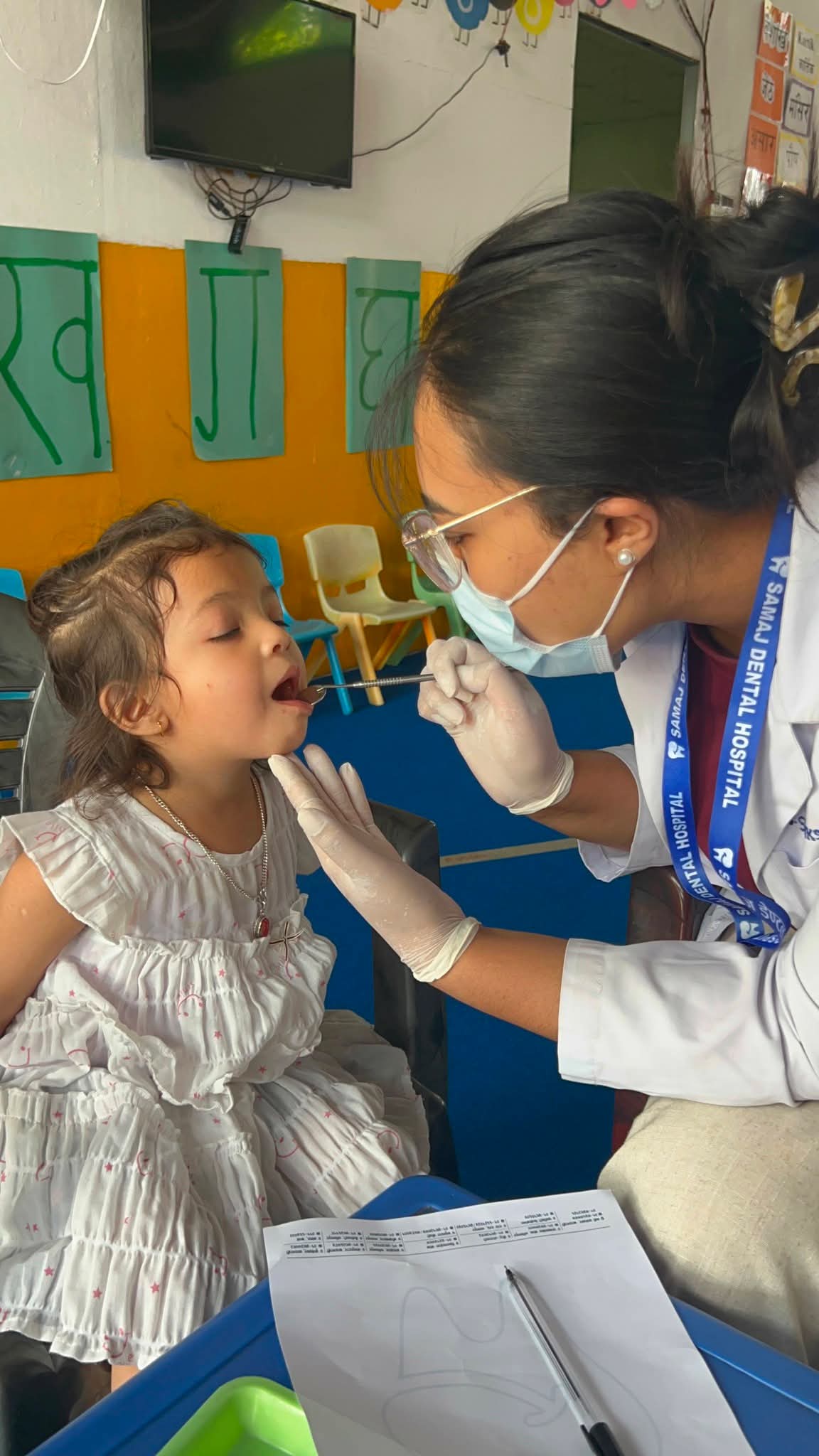A visiting dentist gently checking a student's teeth at school