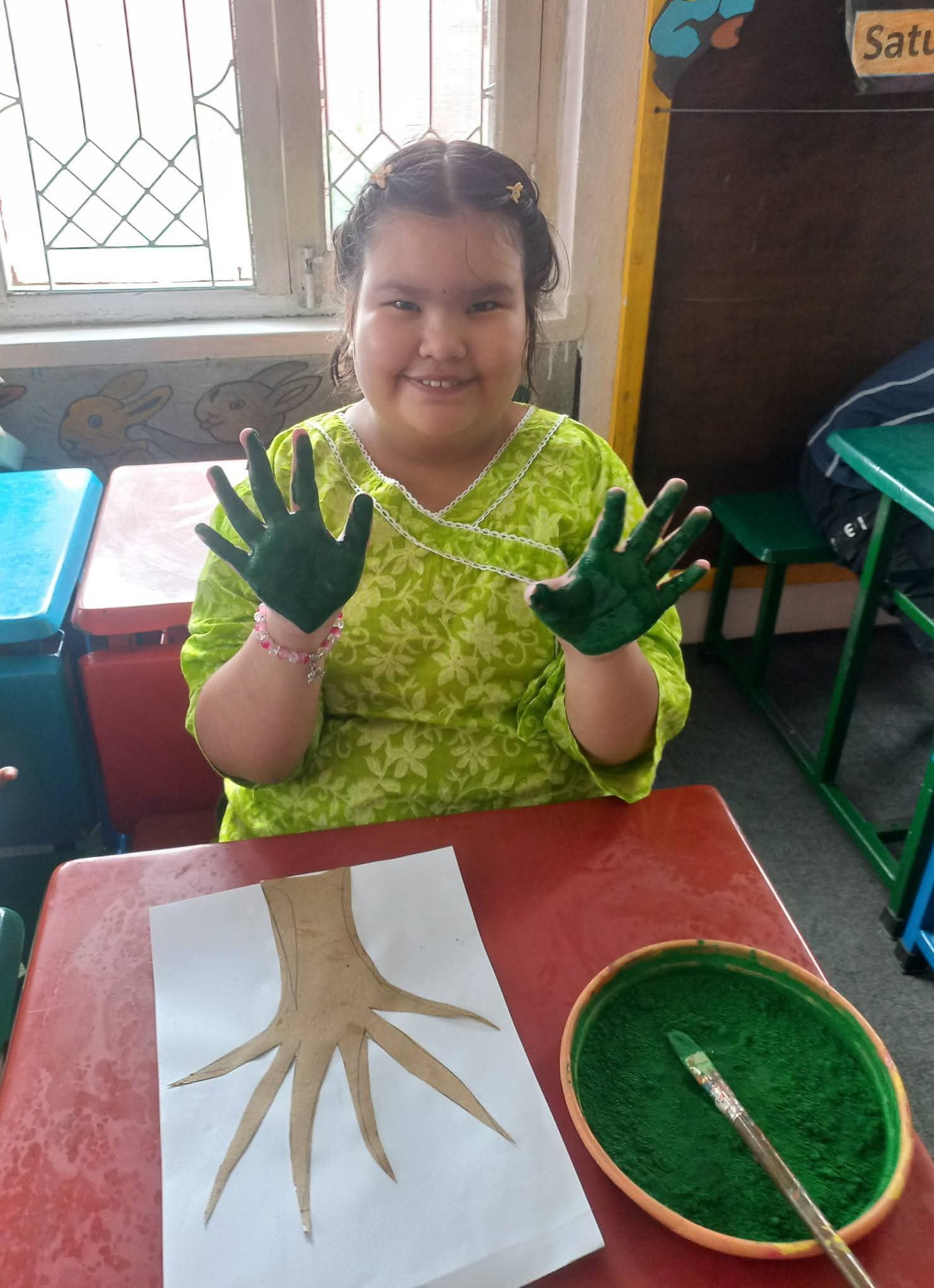 A smiling artist showing her green painted palms above a handprint tree