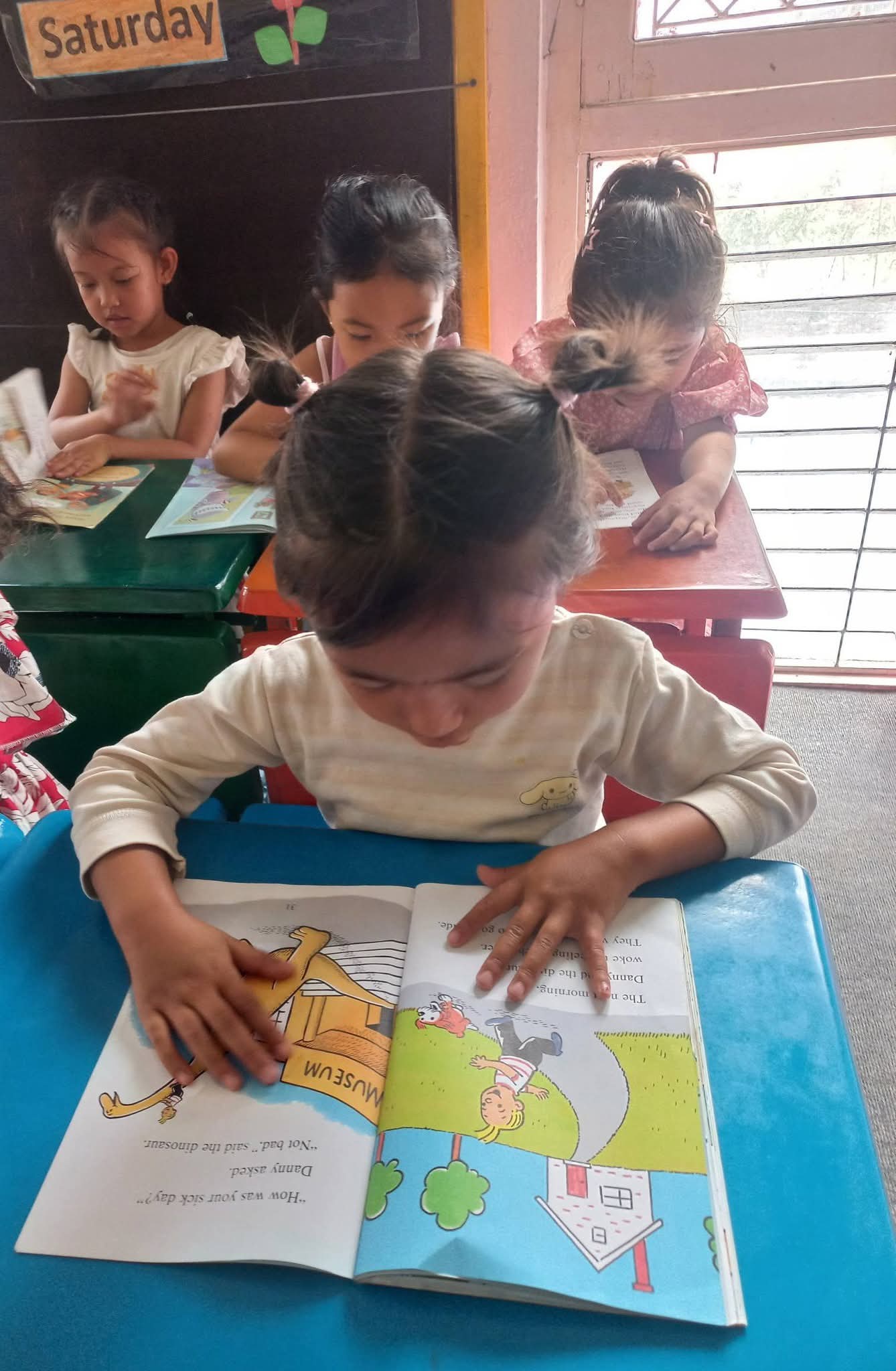 A young reader following a picture book with both hands