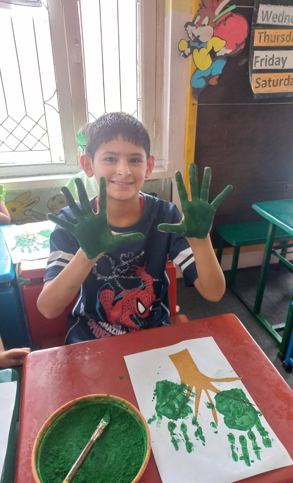 A proud student showing his paint-covered palms beside his handprint tree
