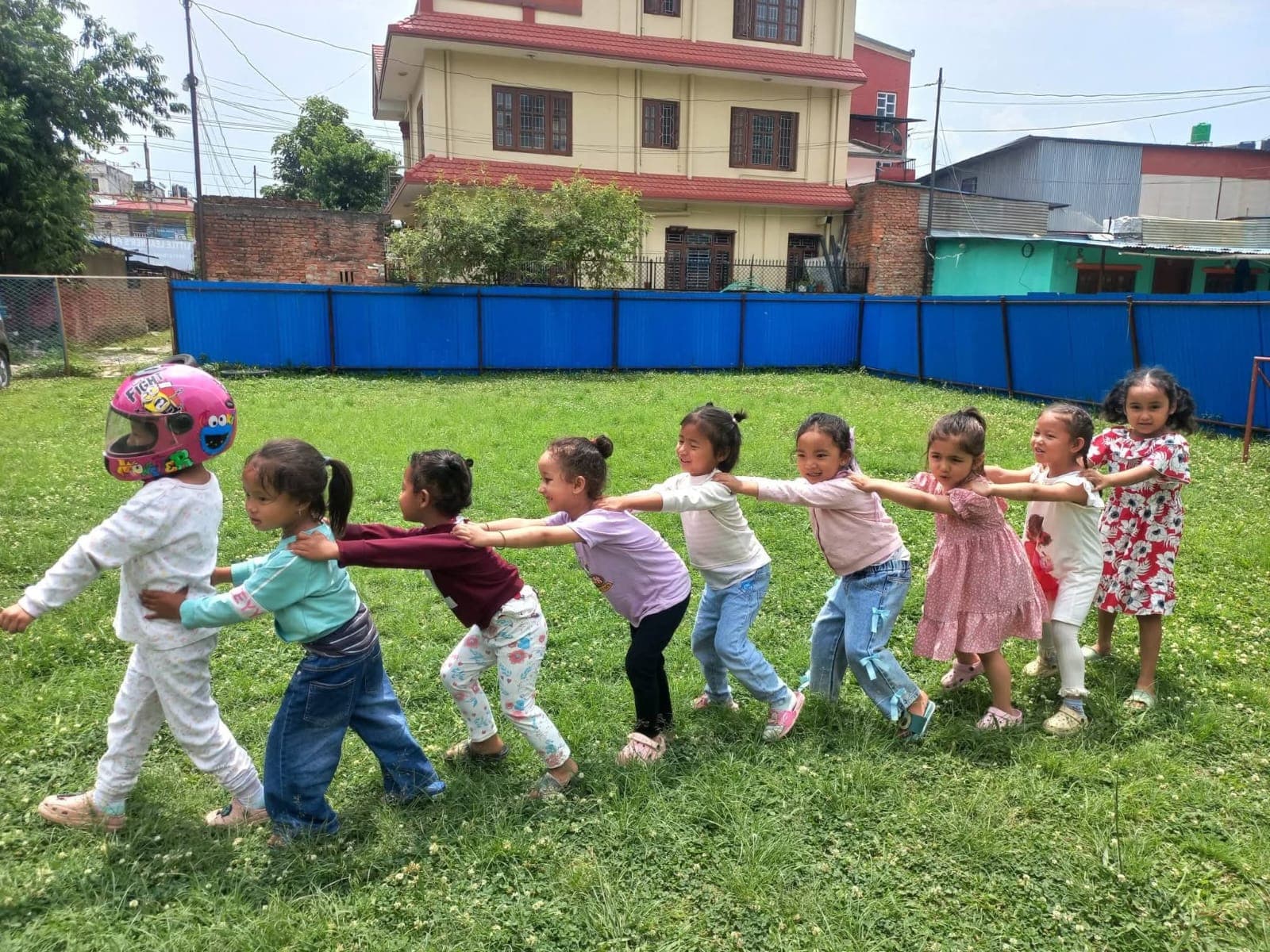 A chain of children holding shoulders, playing train across the lawn